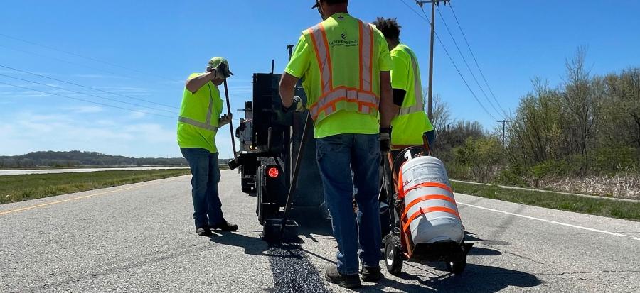 Three men in bright yellow vests while leaning crack seal