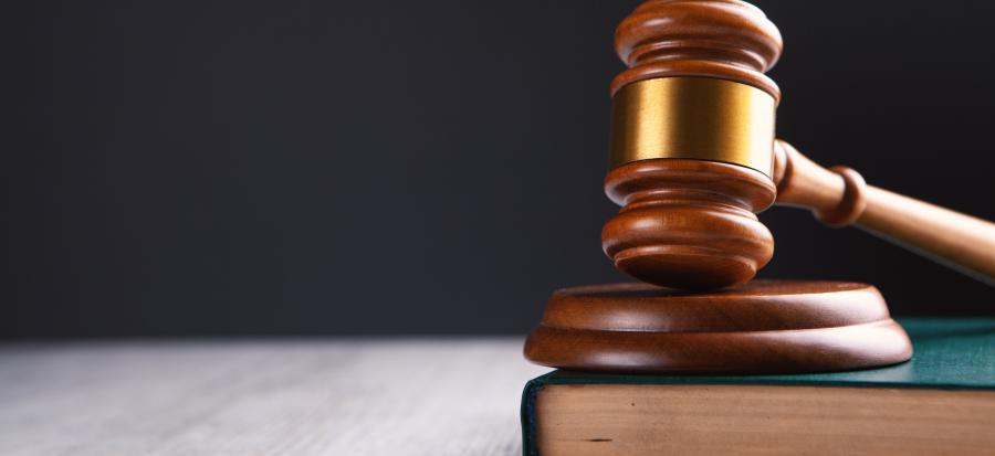 A wooden gavel rests on top of a green book on a wooden desk.