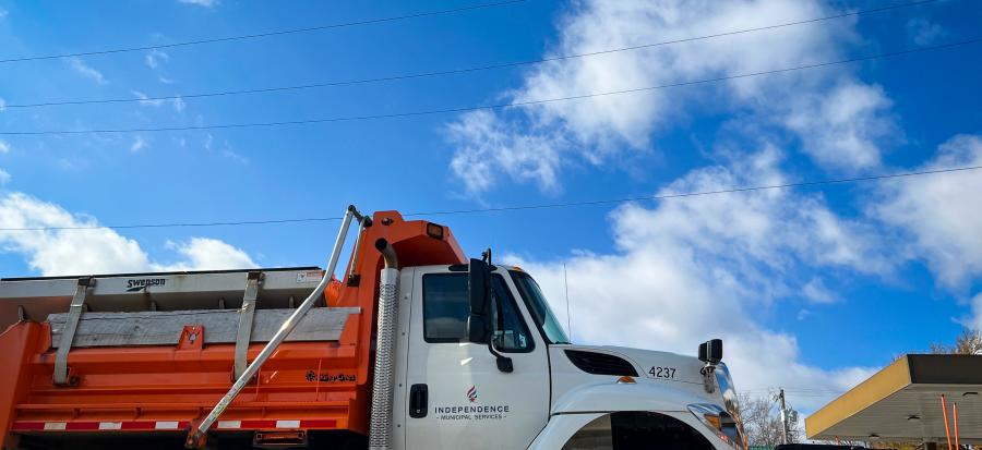 A snow plow with a bright orange shove on the front is lit from behind by the sun