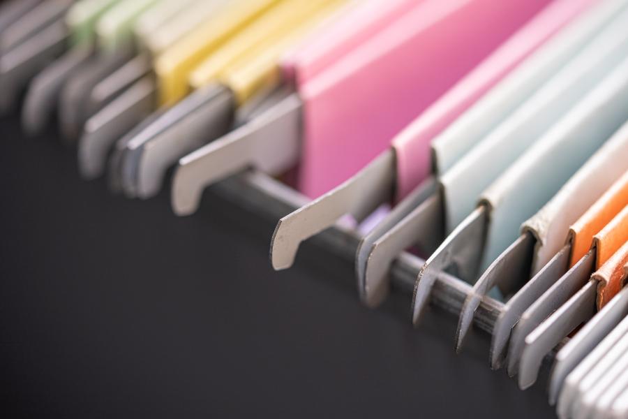 Multiple hanging folders in various colors hang from the side of a drawer.