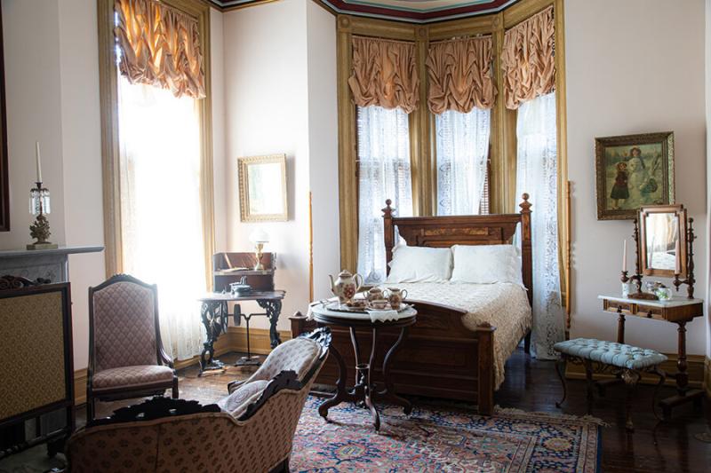 Vaile Mansion guest bedroom with bed, sitting chair and loveseat, tea set, and a small Victorian vanity