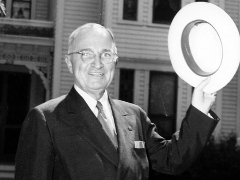 Truman standing outside home with hat in left hand. Independence Truman Home is in the background. 