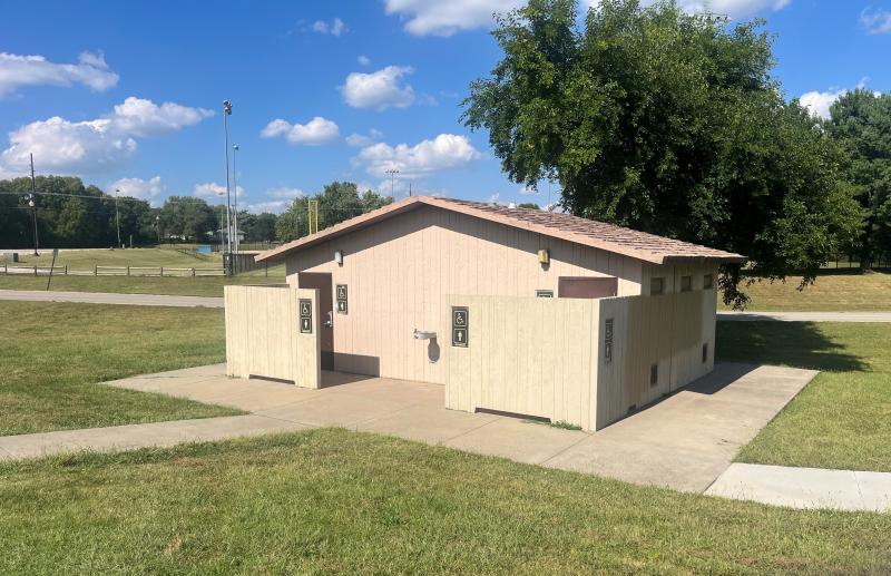 An image of a men's and women's restroom structure surrounded by a sidewalk at Mill Creek Park on a sunny day.