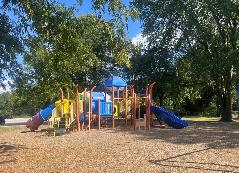 An image of a blue, red and yellow playground area at Mill Creek Park on a sunny day with trees in the background.